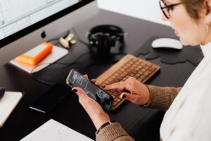 crop woman using smartphone while working at computer